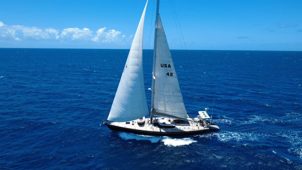 Cap II, a navy-blue-hulled sailing yacht with sail number USA 42, under full sail on blue tropical water.
